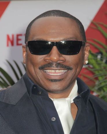 Smiling man wearing dark sunglasses and a suit at an event.