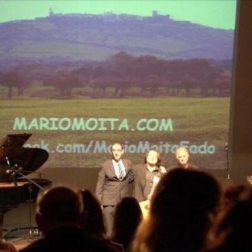 um palco, onde temos um piano de cauda, e do lado direito está mario moita, e mais 2 musicos.publico