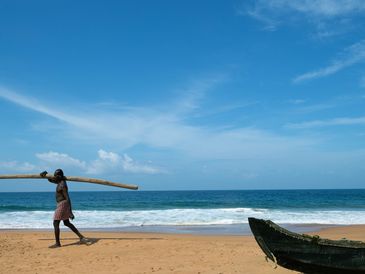 Man walking on the beach with a wooden pole.