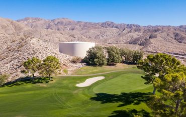 A golf course green near a desert landscape with mountains and a water tank.