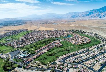 A suburban neighborhood with a golf course surrounded by desert and mountains.
