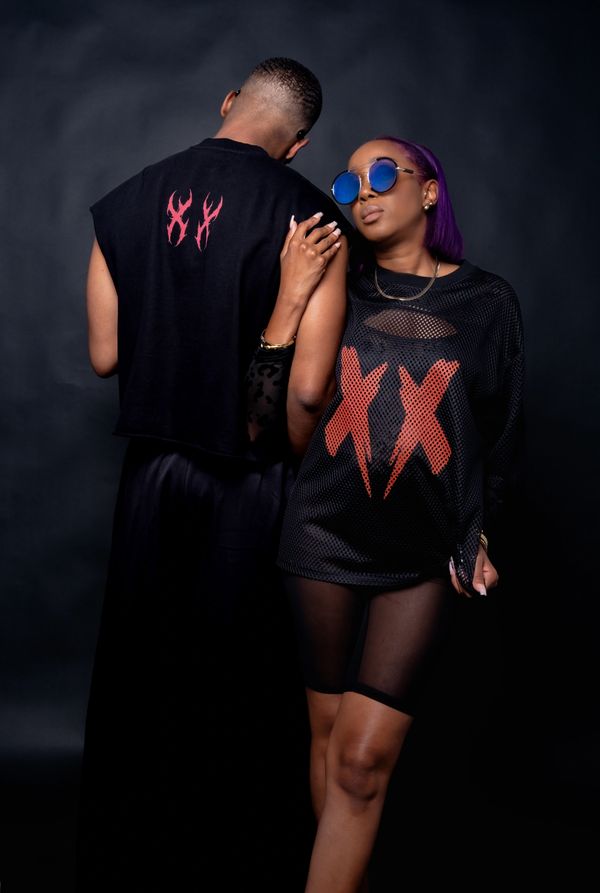 Two fashionably dressed individuals in black outfits with red XX designs.