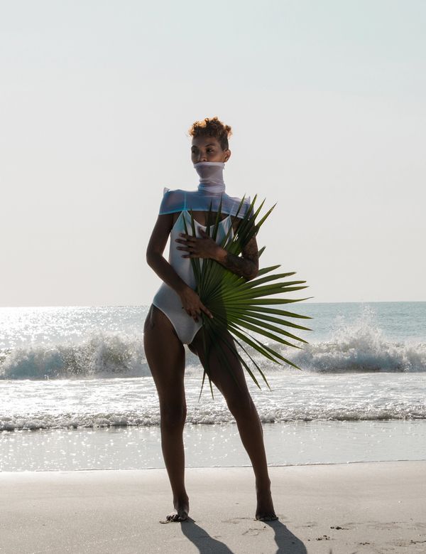 Person in white swimsuit holding a large palm leaf on a sunny beach.