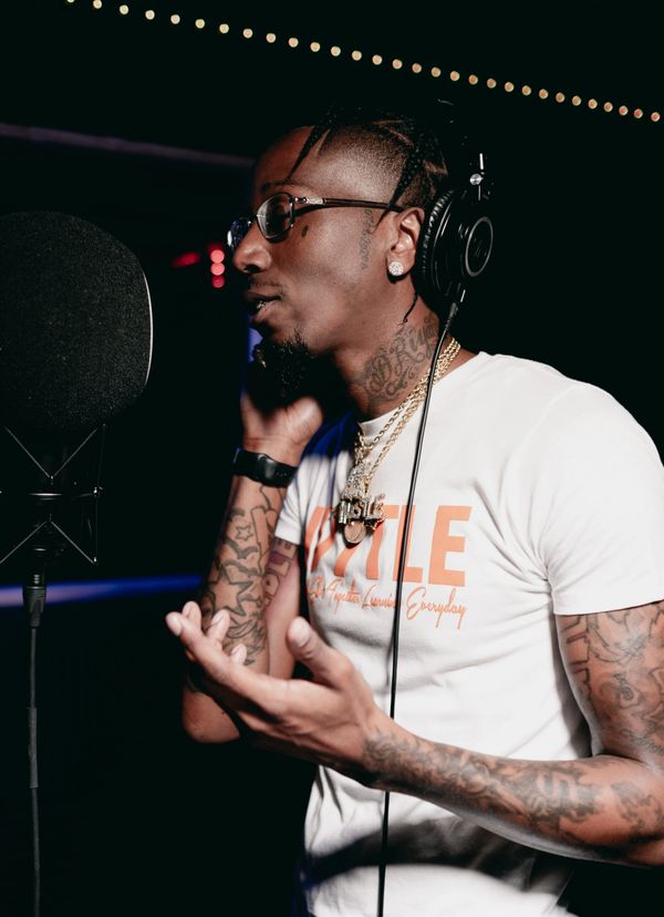 Man with tattoos and glasses recording music in a studio.