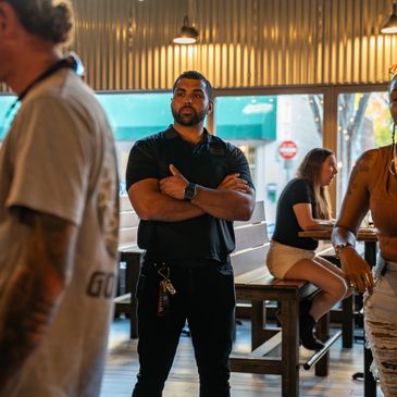 Man in black shirt standing with arms crossed in a casual indoor setting.