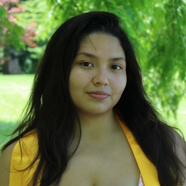 Portrait of a woman with long dark hair outdoors in a green setting.