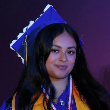 Young woman in graduation attire smiling with a purple background.