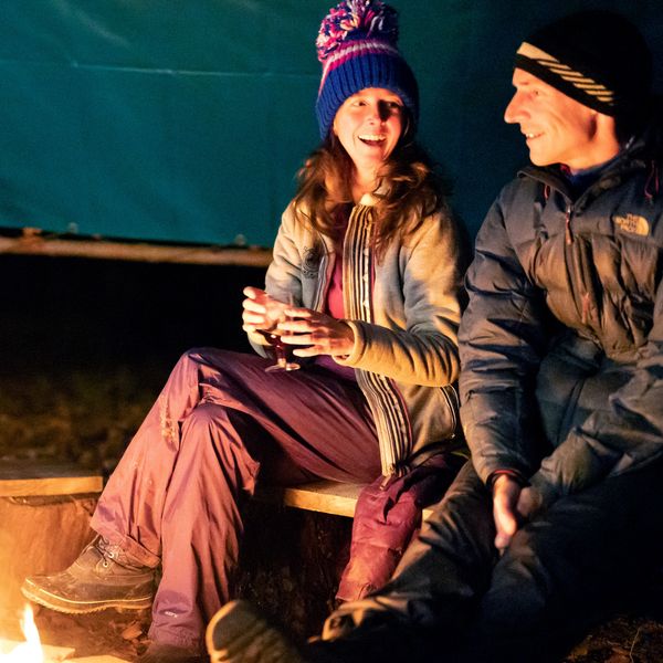 Couple enjoying a drink around winter campfire under shelter at Fat Squirrel Outdoor in Cotswolds
