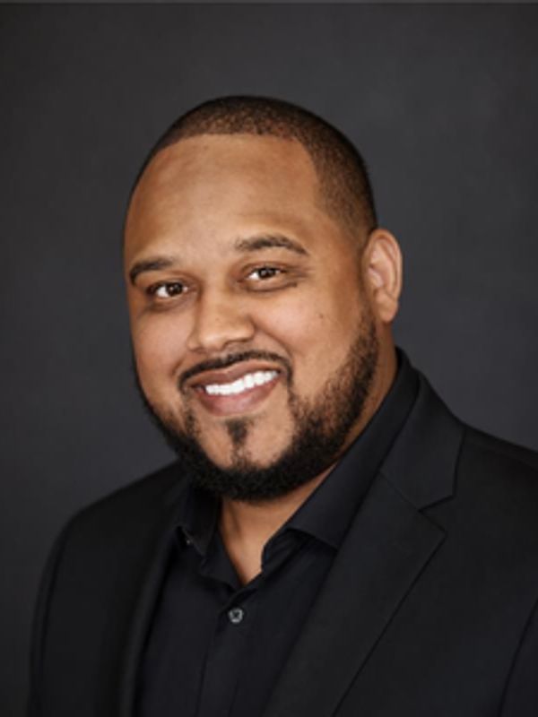 Man smiling in a black suit against a dark background.