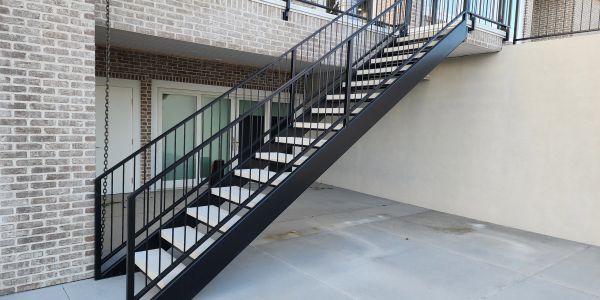 Black metal staircase leading to an upper floor in an outdoor area.