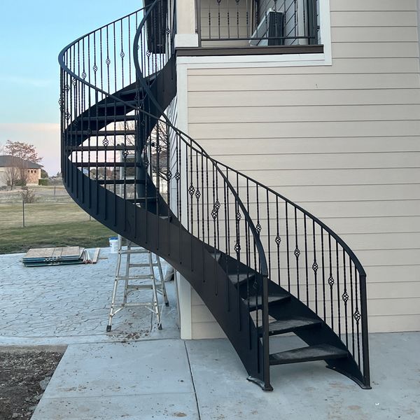 Black metal spiral staircase attached to a white house exterior.