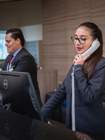 Two professionals working at a reception desk, one on the phone and the other on the computer.