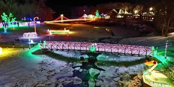 A winter night scene with bridges and trees decorated in colorful holiday lights.