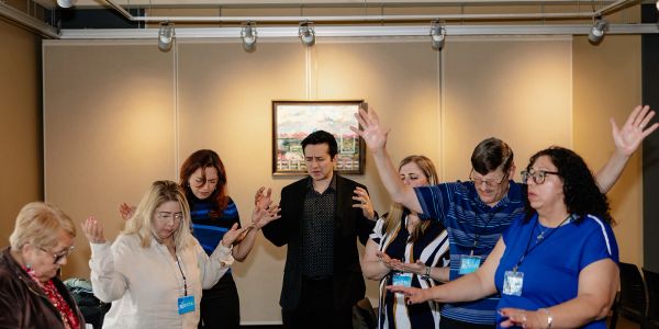 A group of people with eyes closed and hands raised, engaged in a spiritual or prayer session.