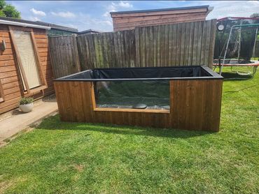 Wooden raised garden bed with a black liner in a backyard.