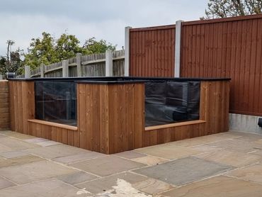 Wooden raised garden bed with glass panels on a stone patio.