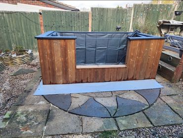 A wooden hot tub with a black interior liner in a backyard setting.