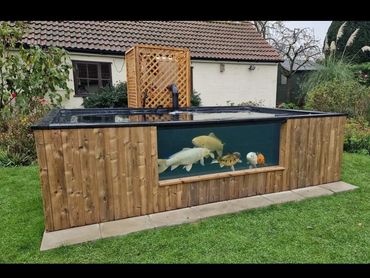 Outdoor wooden fish tank with large koi fish visible through a glass panel.