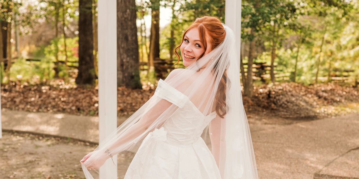 A joyful bride in a white gown and veil smiles outdoors.
