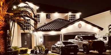 Well-lit house at night with cars parked outside.