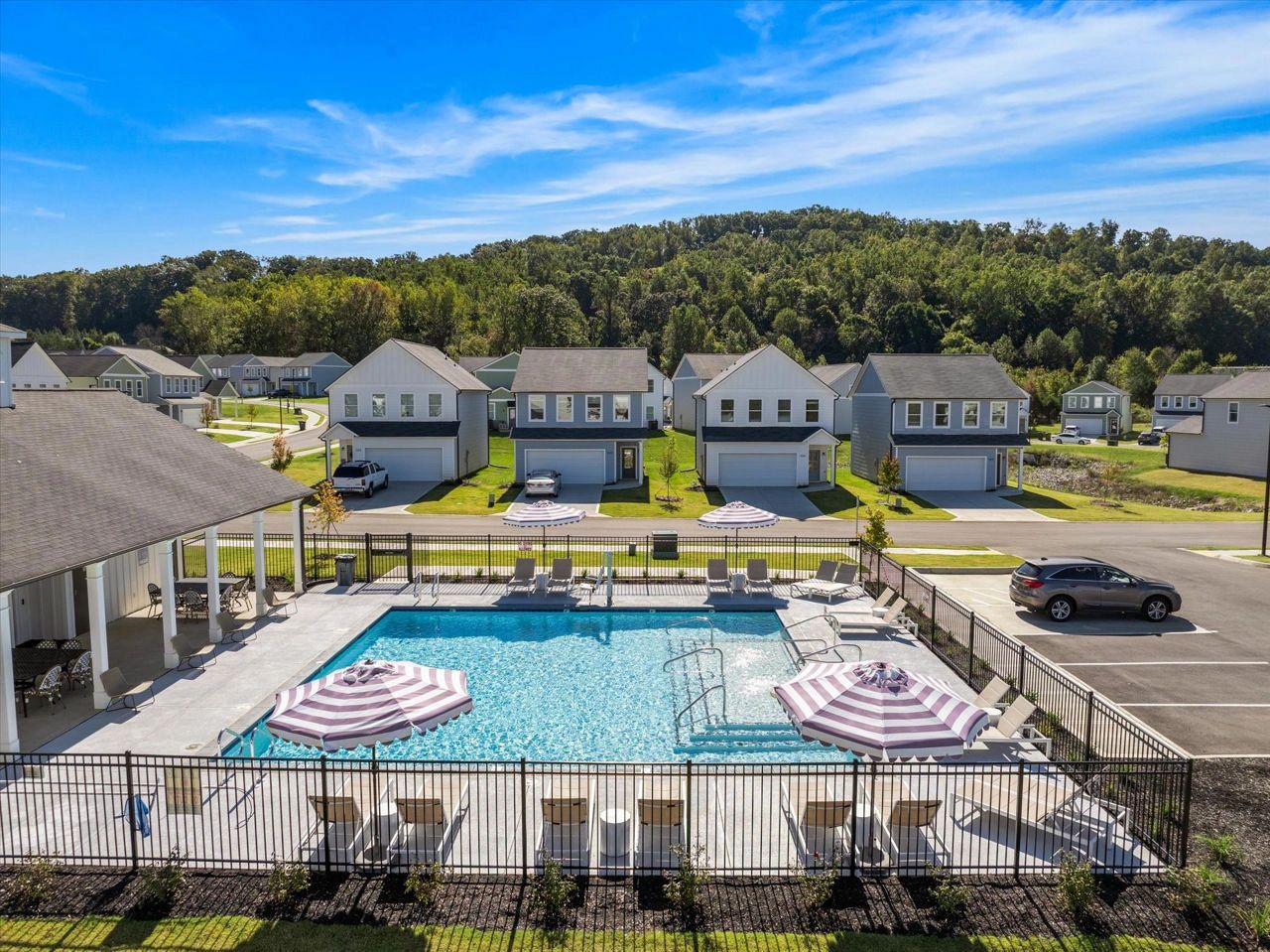 Community pool area with lounge chairs and umbrellas in front of suburban houses.