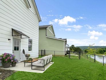 Backyard patio with sofa, grill, and scenic view of green hills and pond.