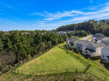 A fenced grassy park area beside suburban houses under a blue sky.