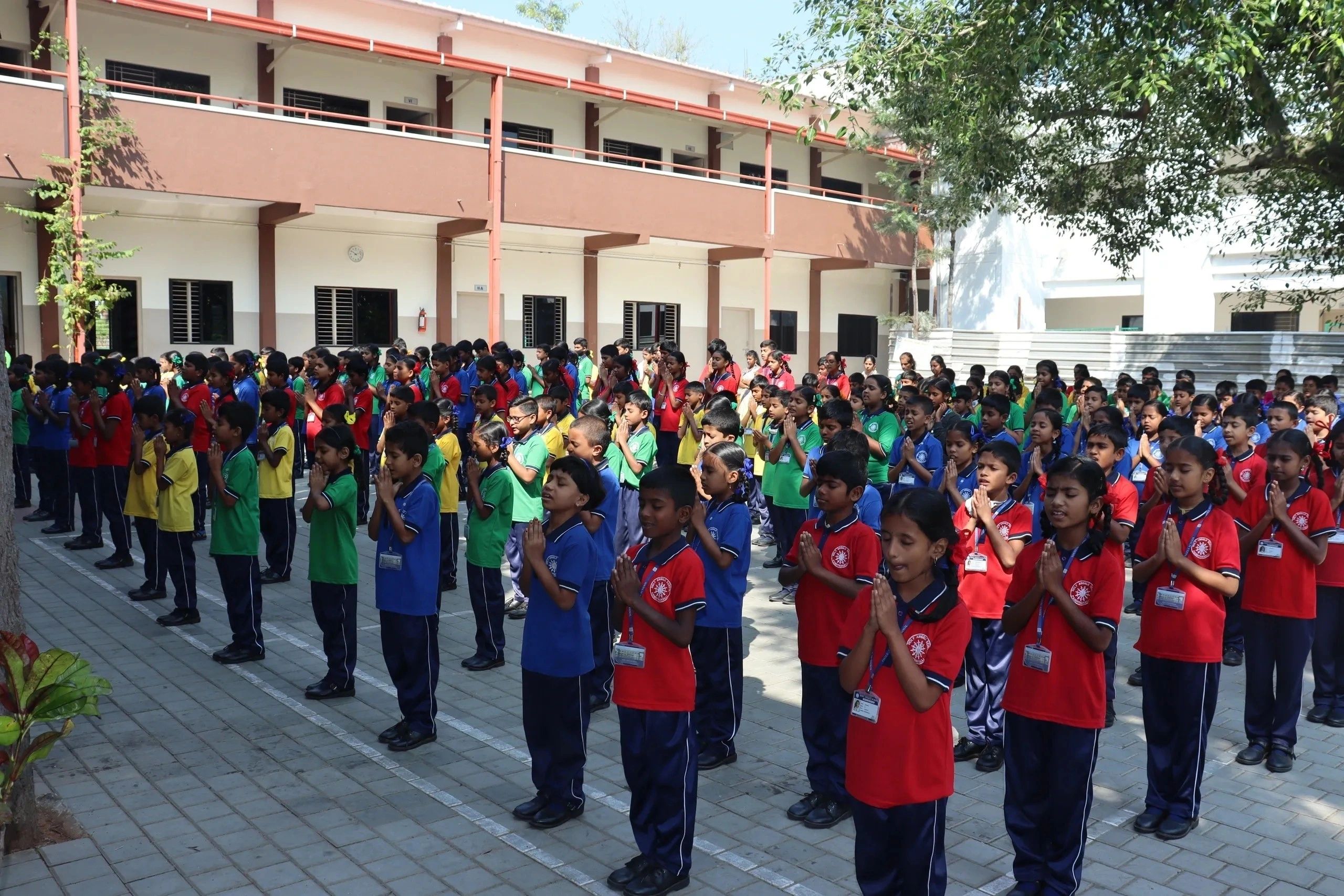 School children standing in prayer outdoors in colorful uniforms.
