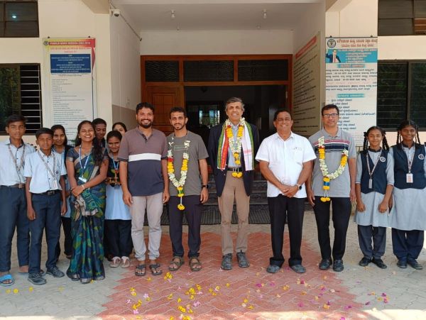 Group photo of students and teachers at a school entrance with garlands and flower petals.