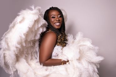 Smiling woman wearing white feathered wings and lace top.