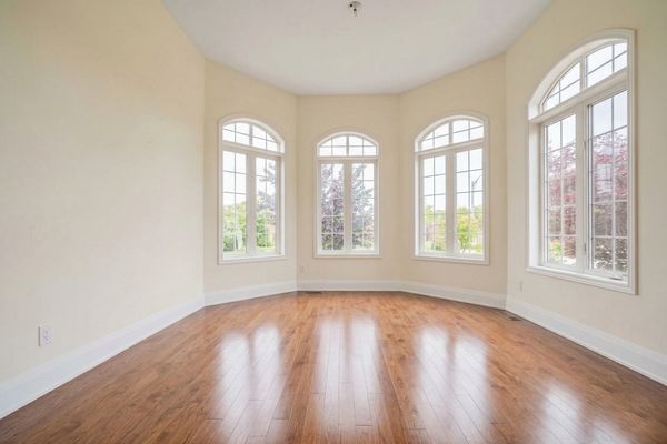Empty room with hardwood floors and large arched windows letting in natural light.