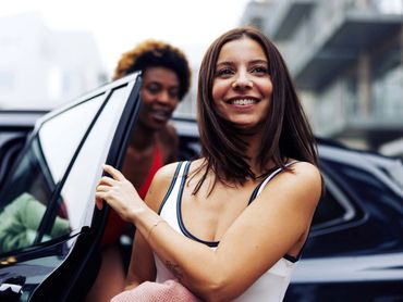Smiling woman getting out of a car with a friend in the background.