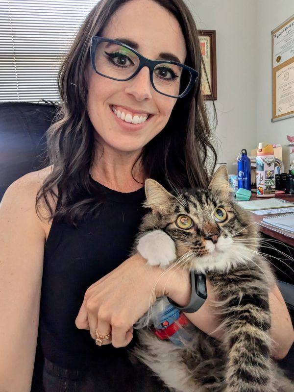 Woman with glasses smiling and holding a tabby cat.