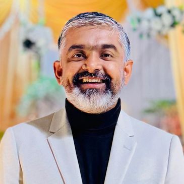 Smiling middle-aged man in a beige blazer and black turtleneck.
