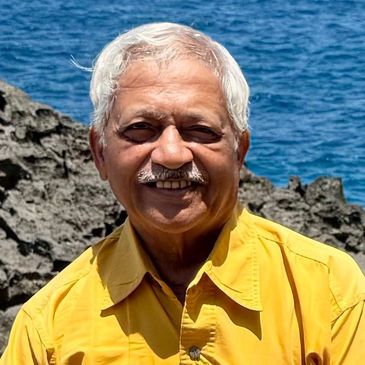 Smiling elderly man in a yellow shirt by the rocky seaside.