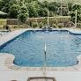 A serene backyard pool surrounded by greenery and a wooden deck.
