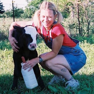 A woman smiles while feeding a calf outdoors on a sunny day.