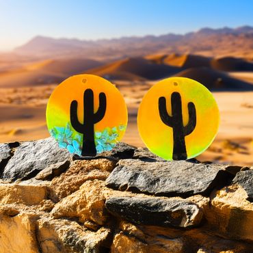 2 Southwestern 3.5 inch ornaments of a cactus in center with orange/yellow sunset and turquoise rocks