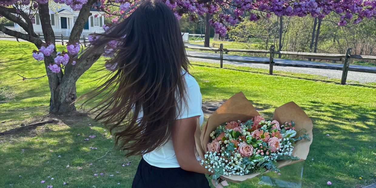Woman with long hair holding a bouquet of flowers under a blooming tree.