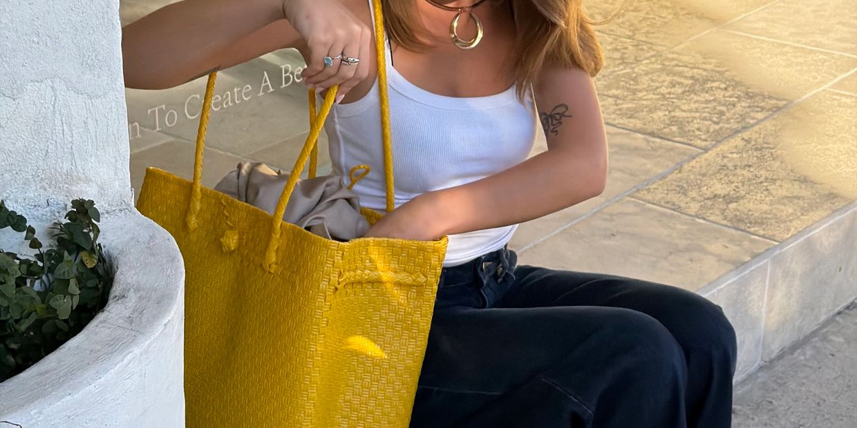 Woman in white top holding a large yellow woven bag while sitting.