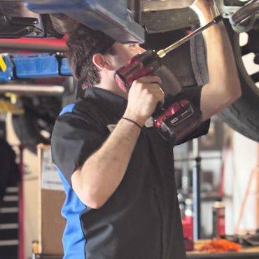 Mechanic using a power drill to work under a raised vehicle in a garage.