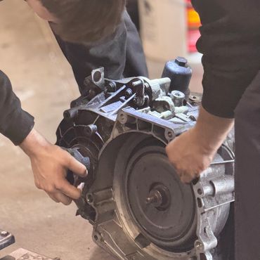 Two people working on a large mechanical part, possibly an engine or transmission.