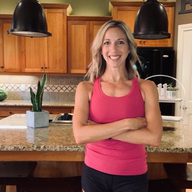 A smiling blonde woman stands in front of her kitchen island with her arms crossed.