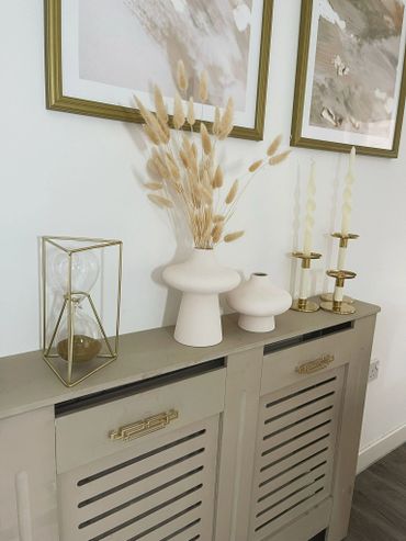 Minimalist decor with vases, candles, and an hourglass on a beige cabinet.