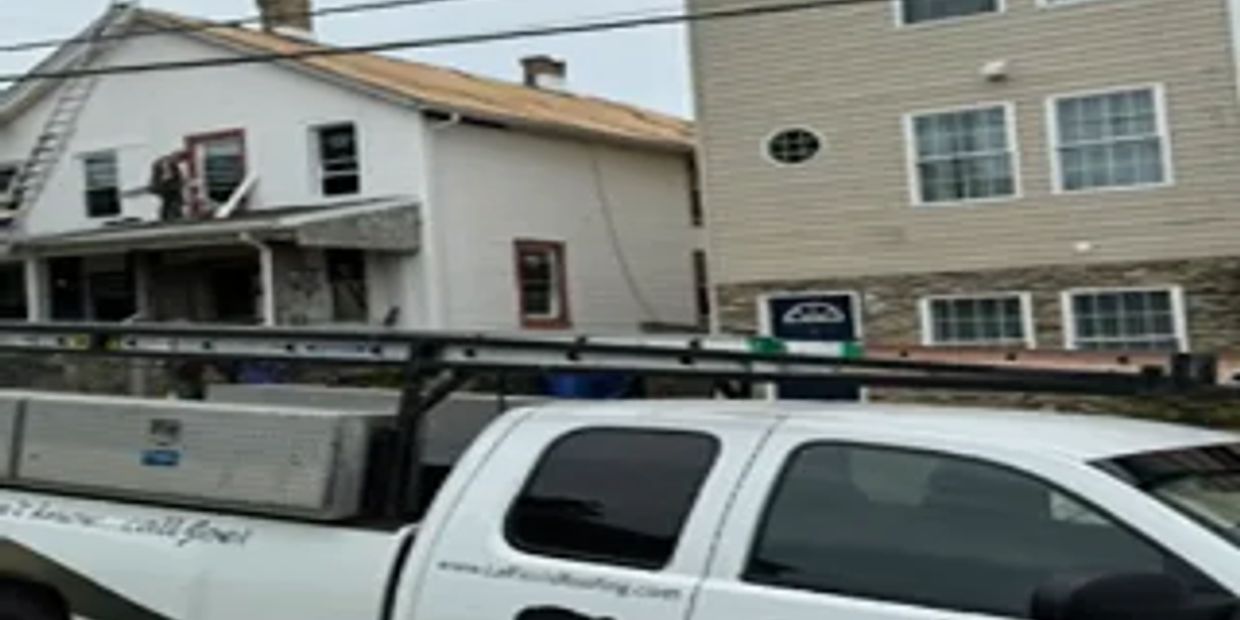 A white work truck with ladders in front of two houses.