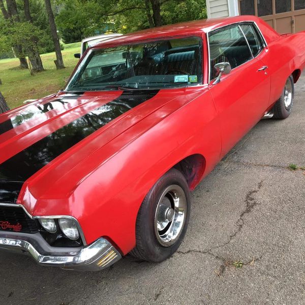 Classic red muscle car with black racing stripes parked on a driveway.