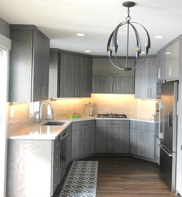 Modern kitchen with gray cabinets, wood flooring, and stylish chandelier.