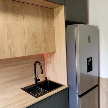 Modern kitchen corner with black sink and stainless steel refrigerator.