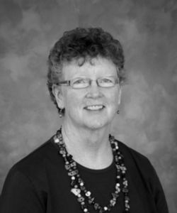 Black and white portrait of a smiling woman with curly hair and glasses.