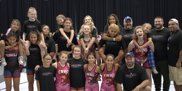 A group photo of young female athletes and their coaches in a gym.